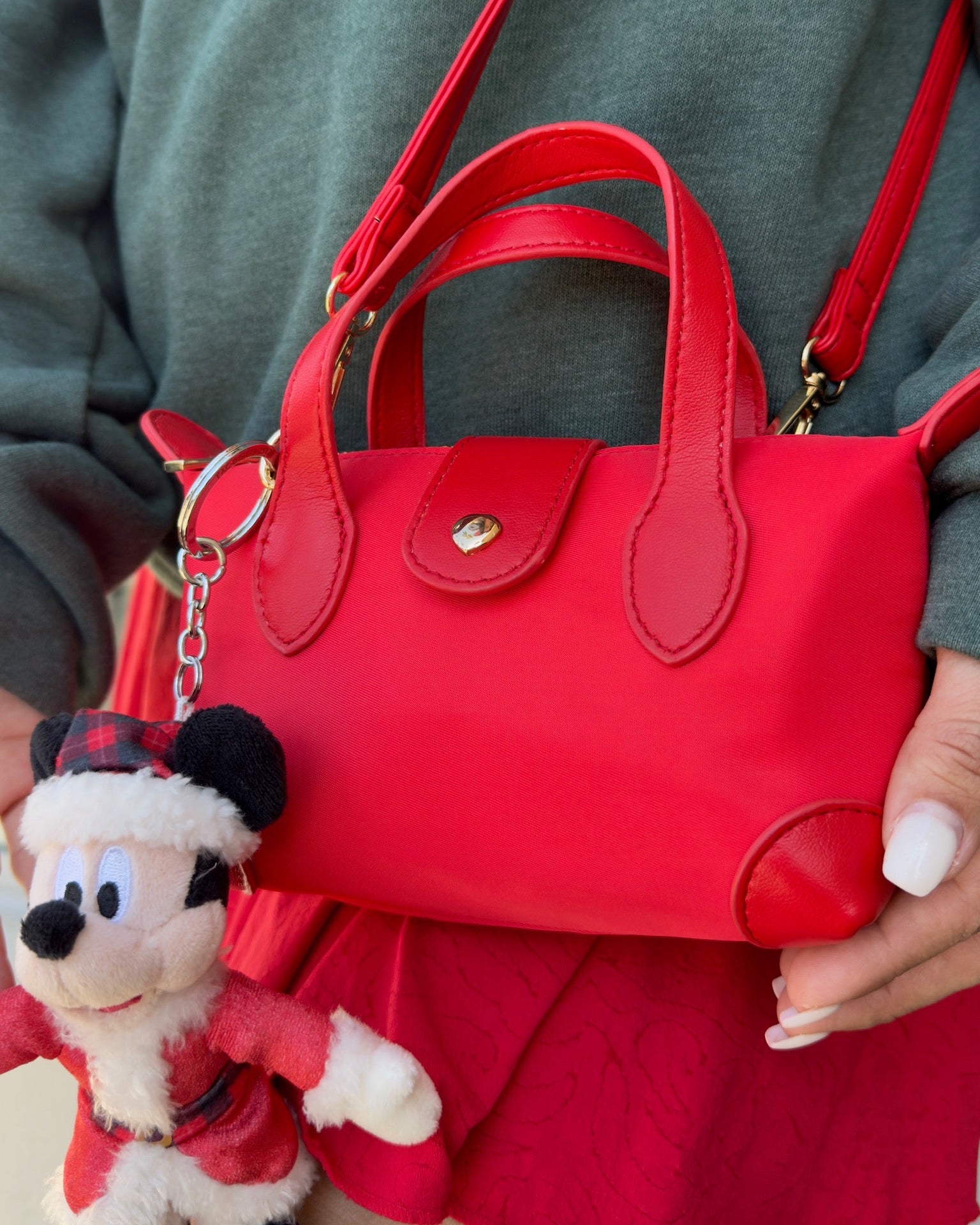 Red handbag held by a person with a Santa-themed keychain attached, on a neutral background.