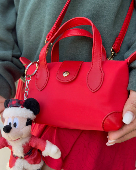 Red handbag held by a person with a Santa-themed keychain attached, on a neutral background.