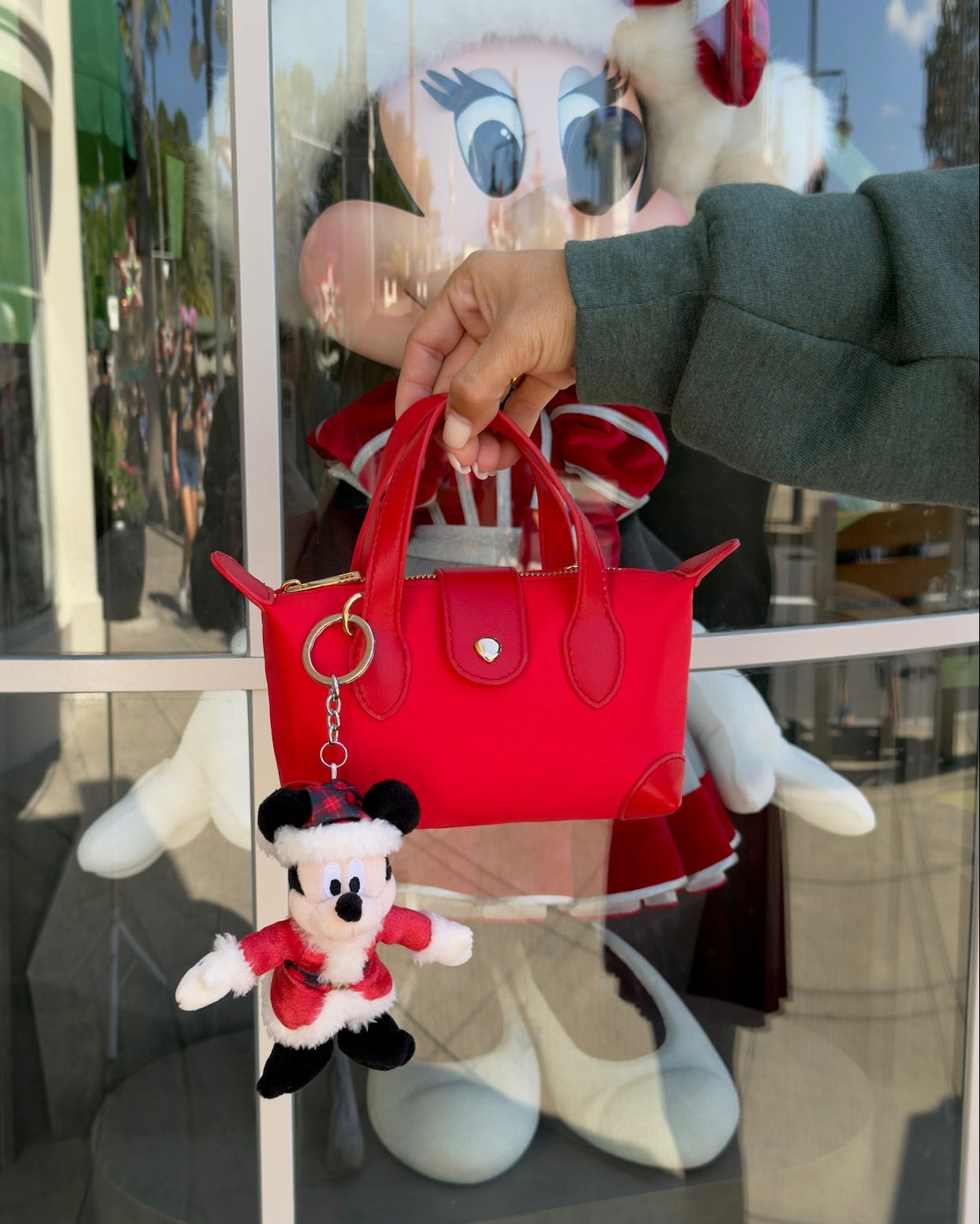 Red handbag with a matching keychain held by a person in front of a cartoon character.
