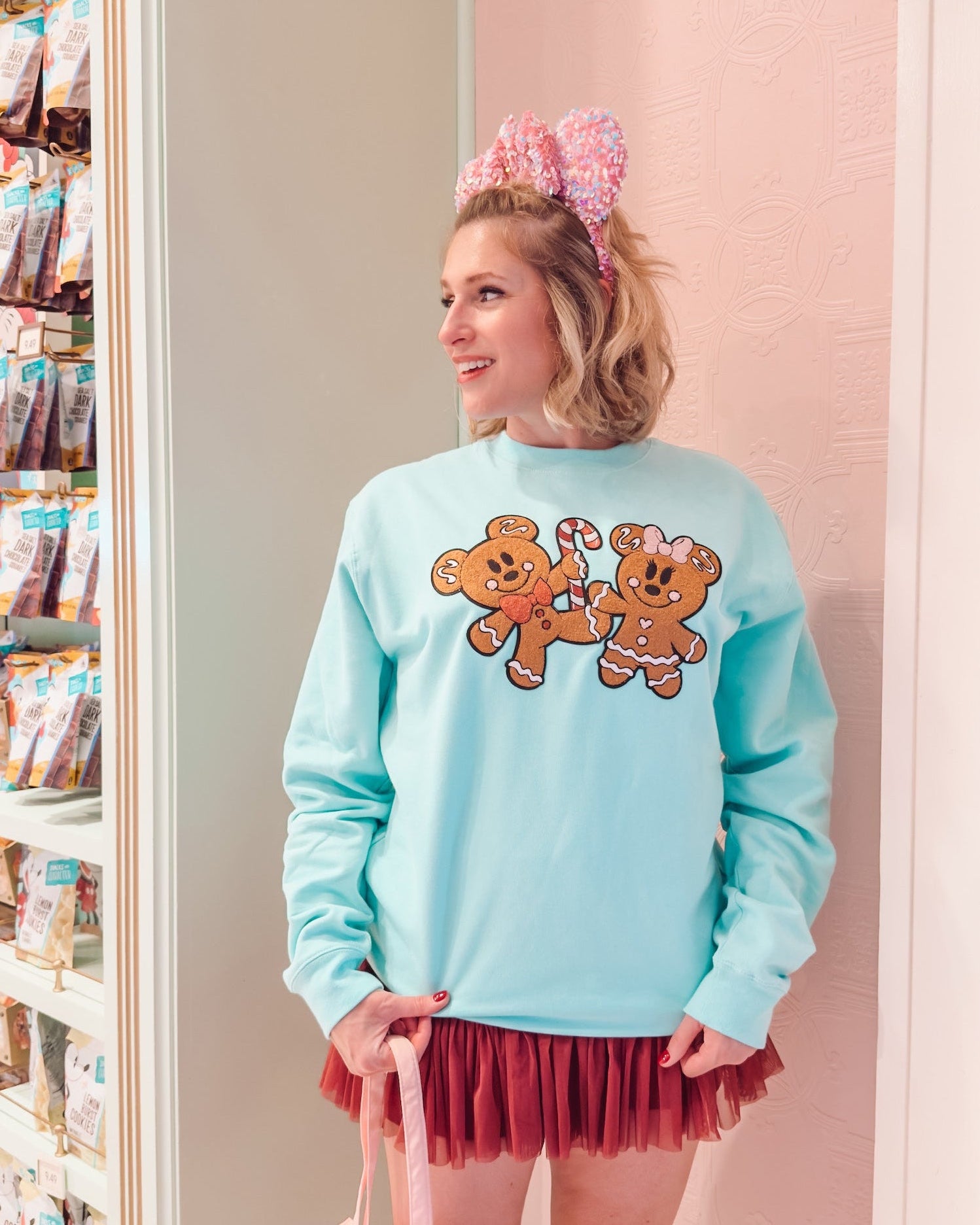Person wearing a light blue sweatshirt with teddy bear graphics, pink bunny ears, and a red skirt in a store.