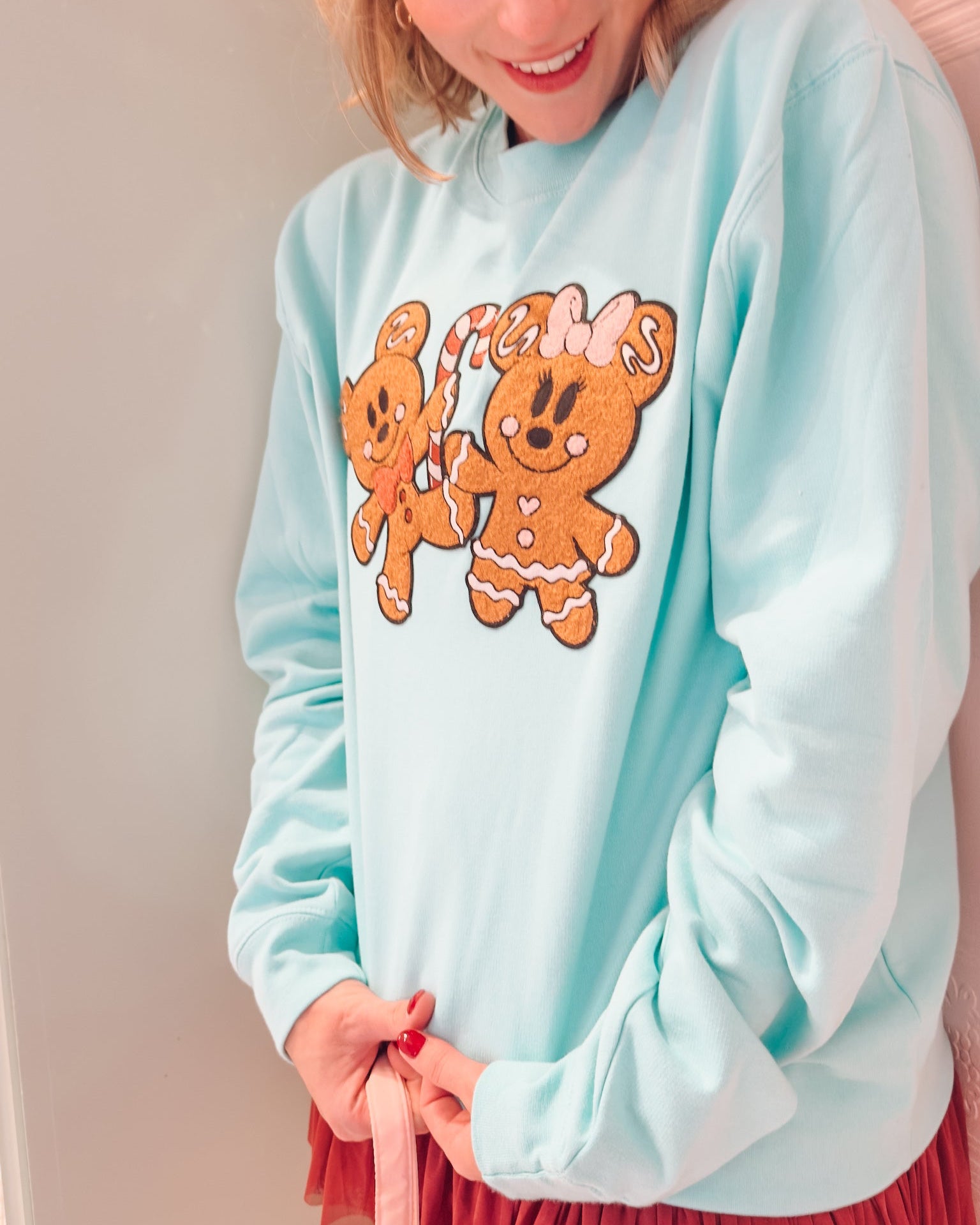 Person wearing a light blue sweatshirt with gingerbread man design, standing against a neutral background.