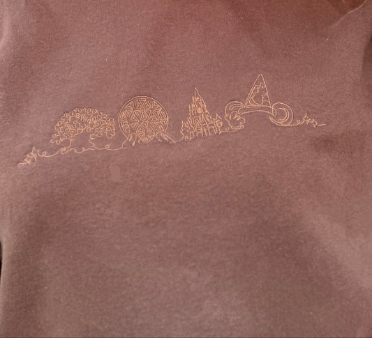 Person wearing a brown sweatshirt with embroidered designs, sunglasses, and colorful headband.